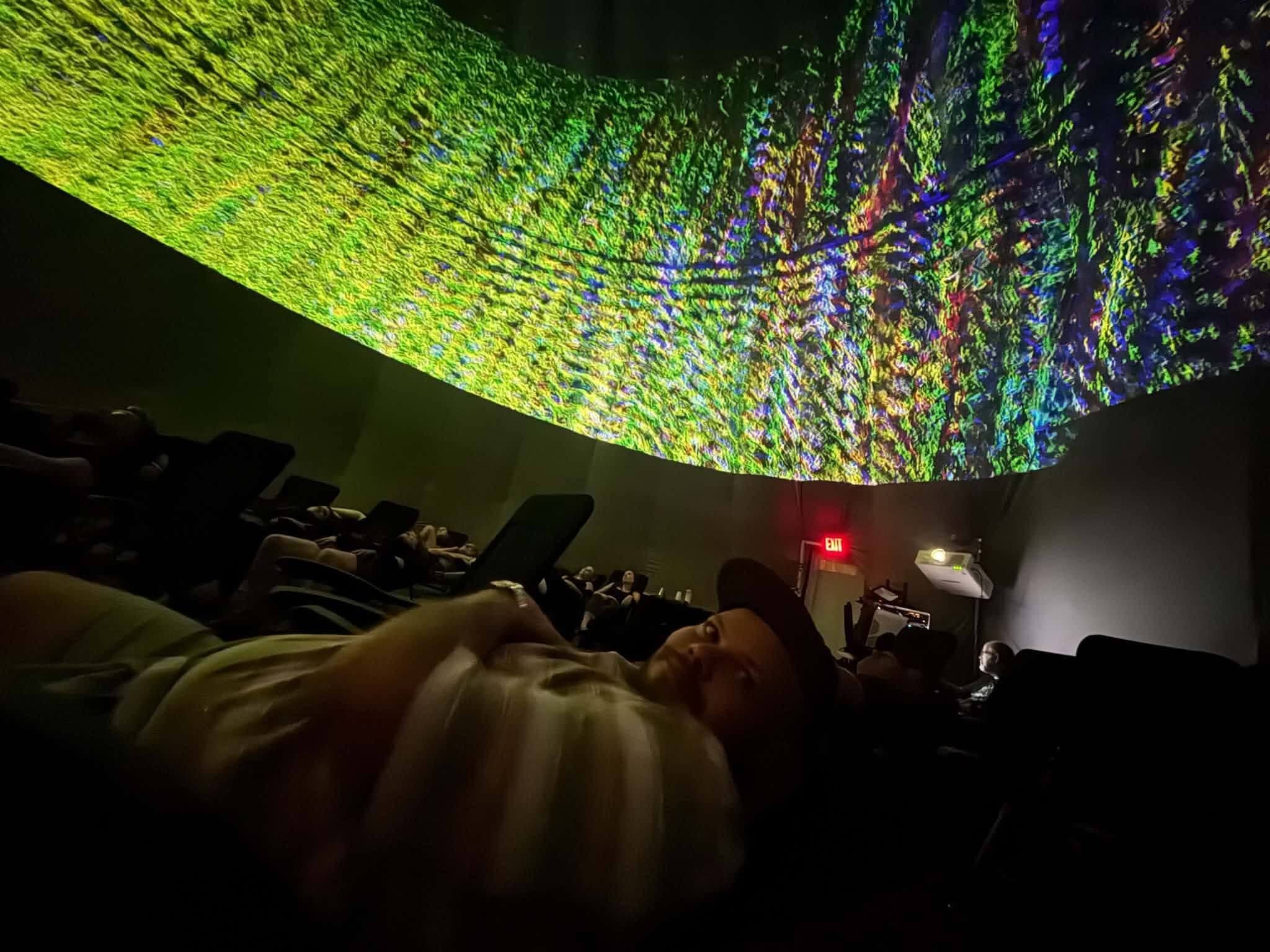 Reclining guests watch a band of green and gold streaks race around the dome